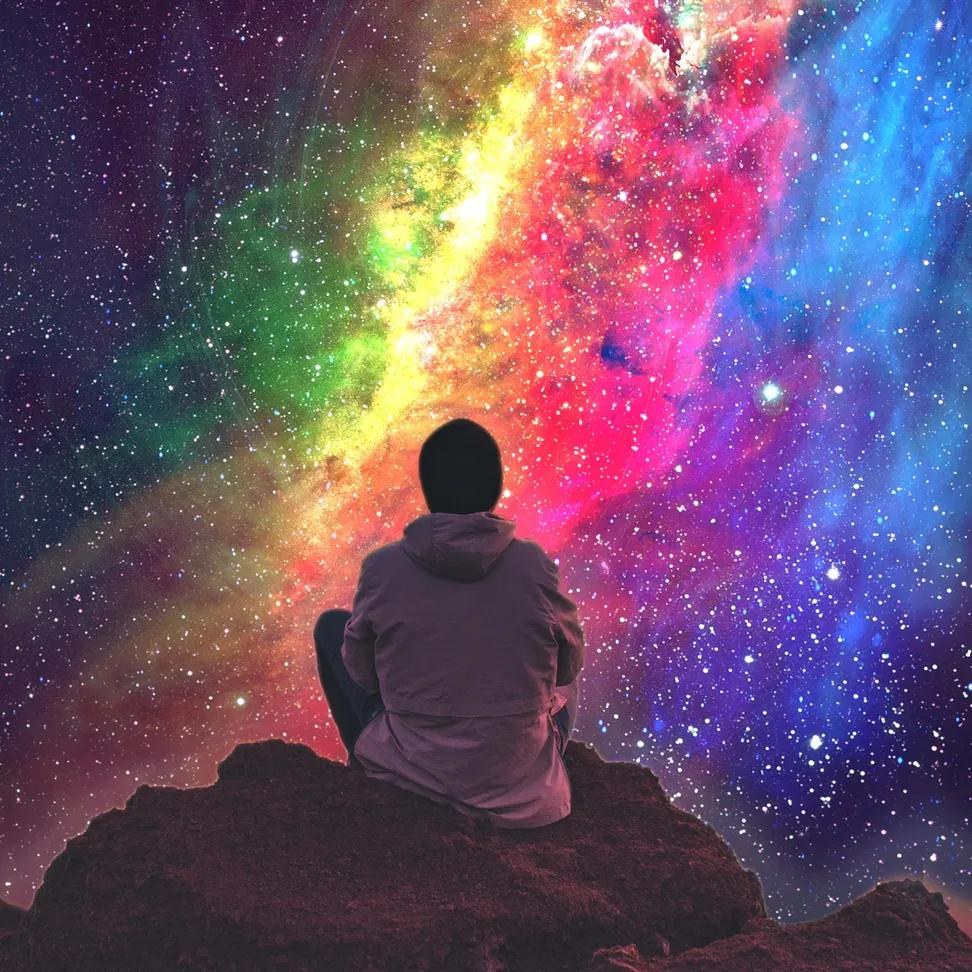 The Colour of Everything — a silhouetted figure sits on a rock before a vast rainbow cosmos, The Luminous Wilds biome